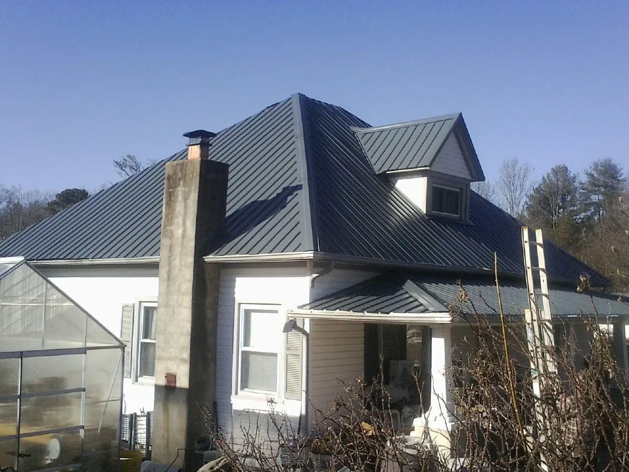 Dark blue standing seam metal roof on a white farmhouse with dormer — Slate & Tile Roof Repair by Roofing Brothers in Dekalb