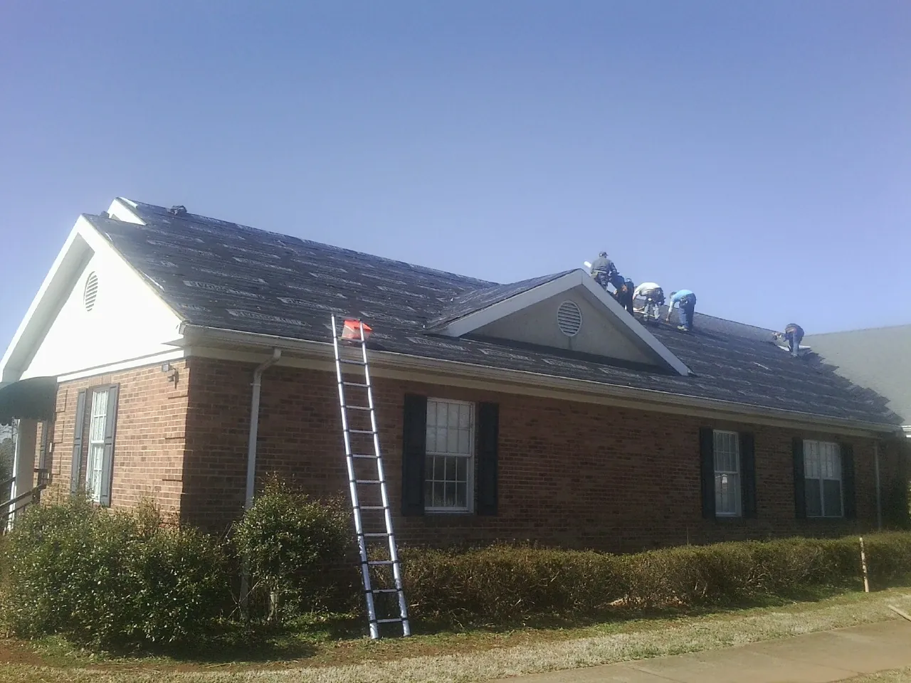 Crew tearing shingles off a brick ranch roof with a ladder set — Emergency Roof Repair work by our crew in Dekalb