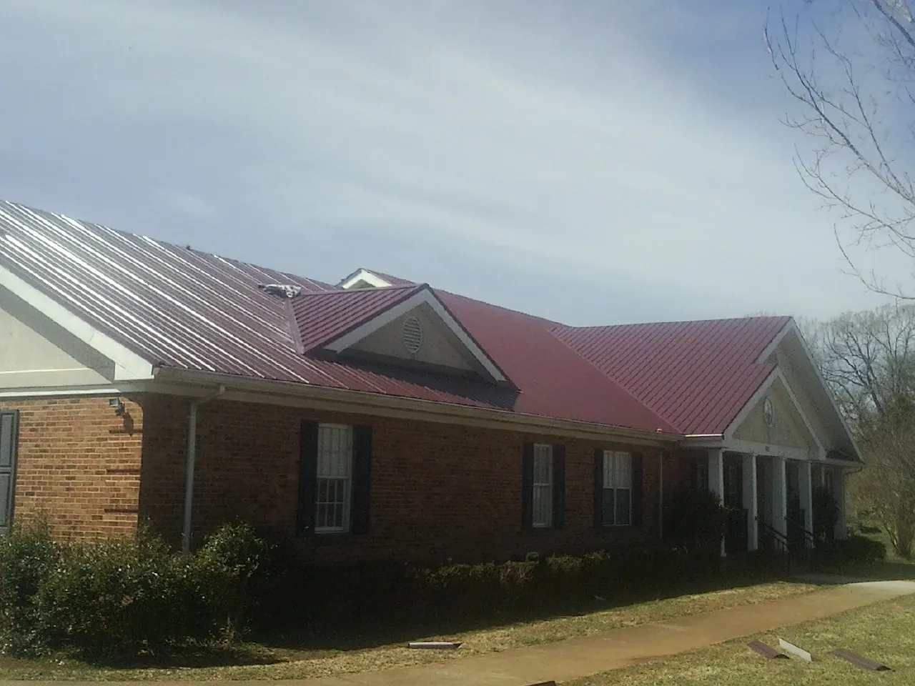 Red metal roof with gabled entries on a long brick building, from a Hail Damage Roof Repair job in Dekalb