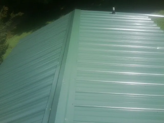 New green metal panels meeting at the ridge of a roof — Flat Roof Repair work by our crew in Dekalb