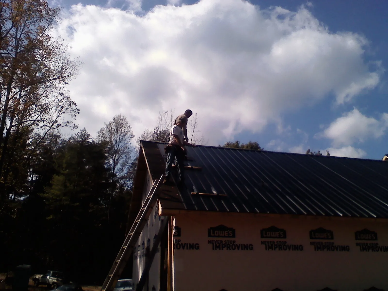 Roofer fastening dark metal panels high against a cloudy sky, from a Roof Inspection job in Dekalb