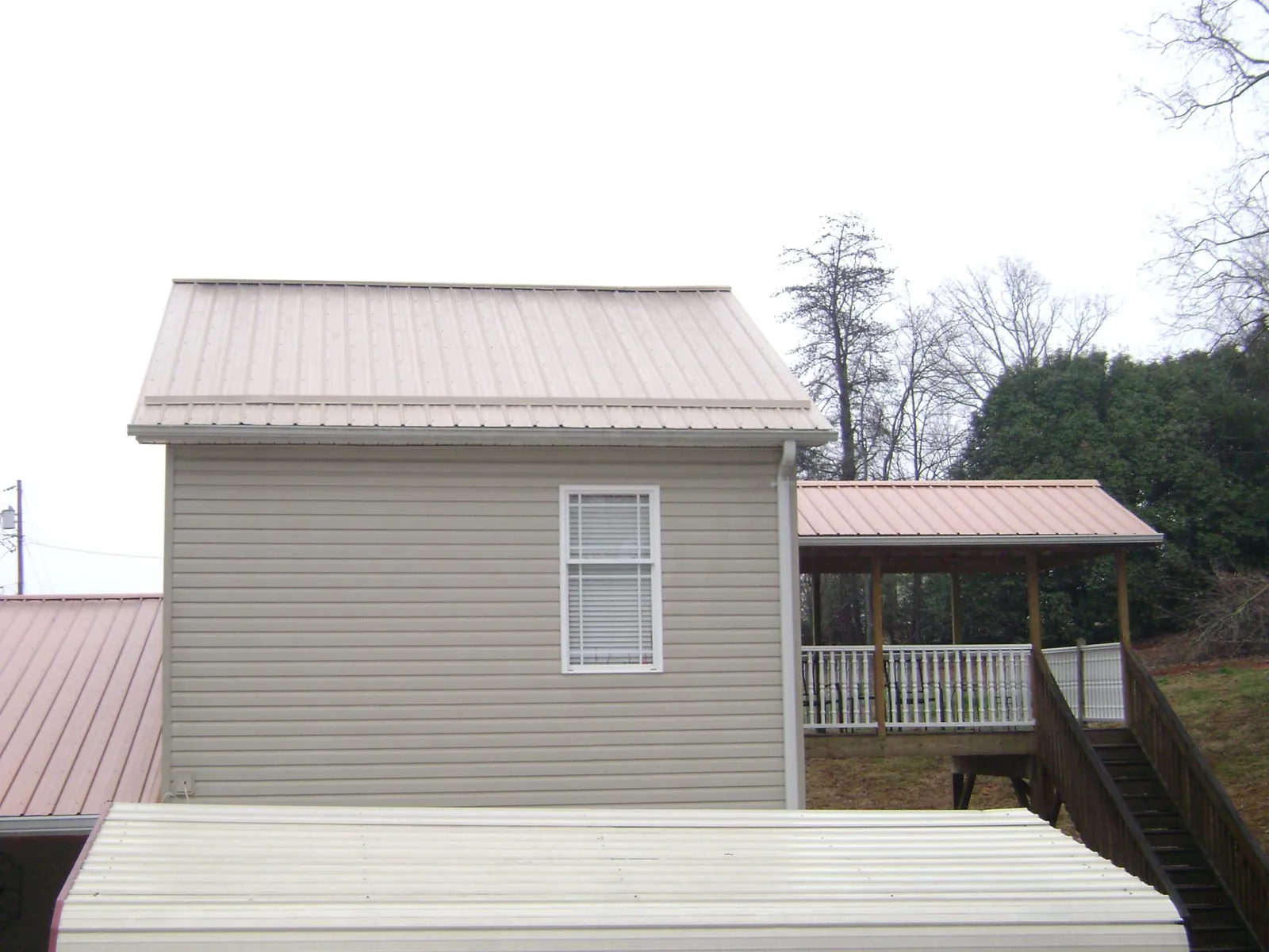 Tan metal roofs on a two story addition and attached porch, from a Roof Replacement job in Dekalb
